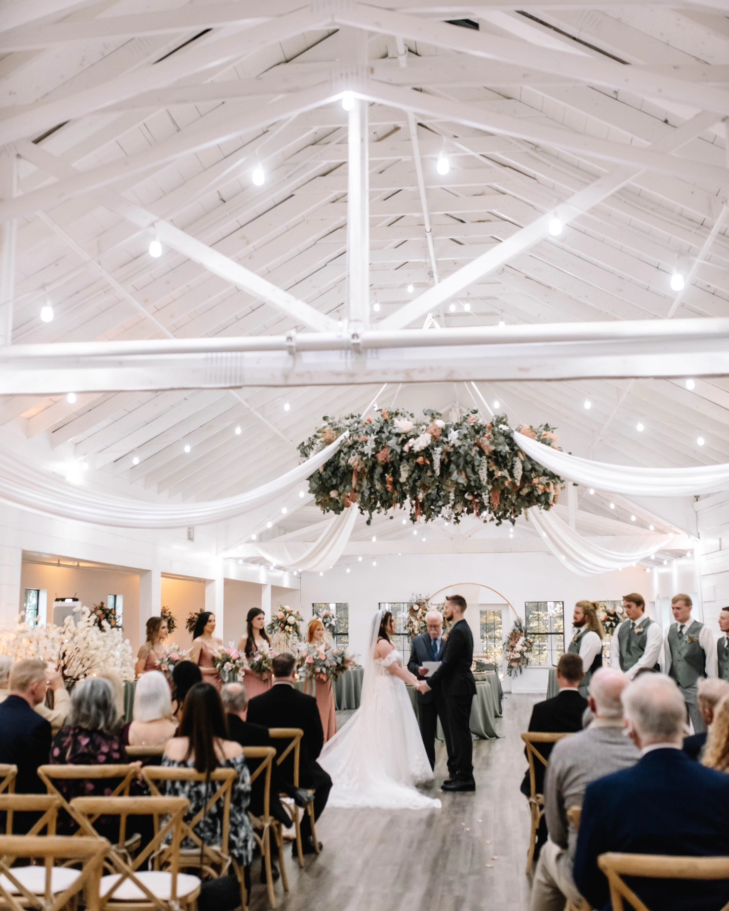 bride and groom saying vows under large hanging floral arrangement