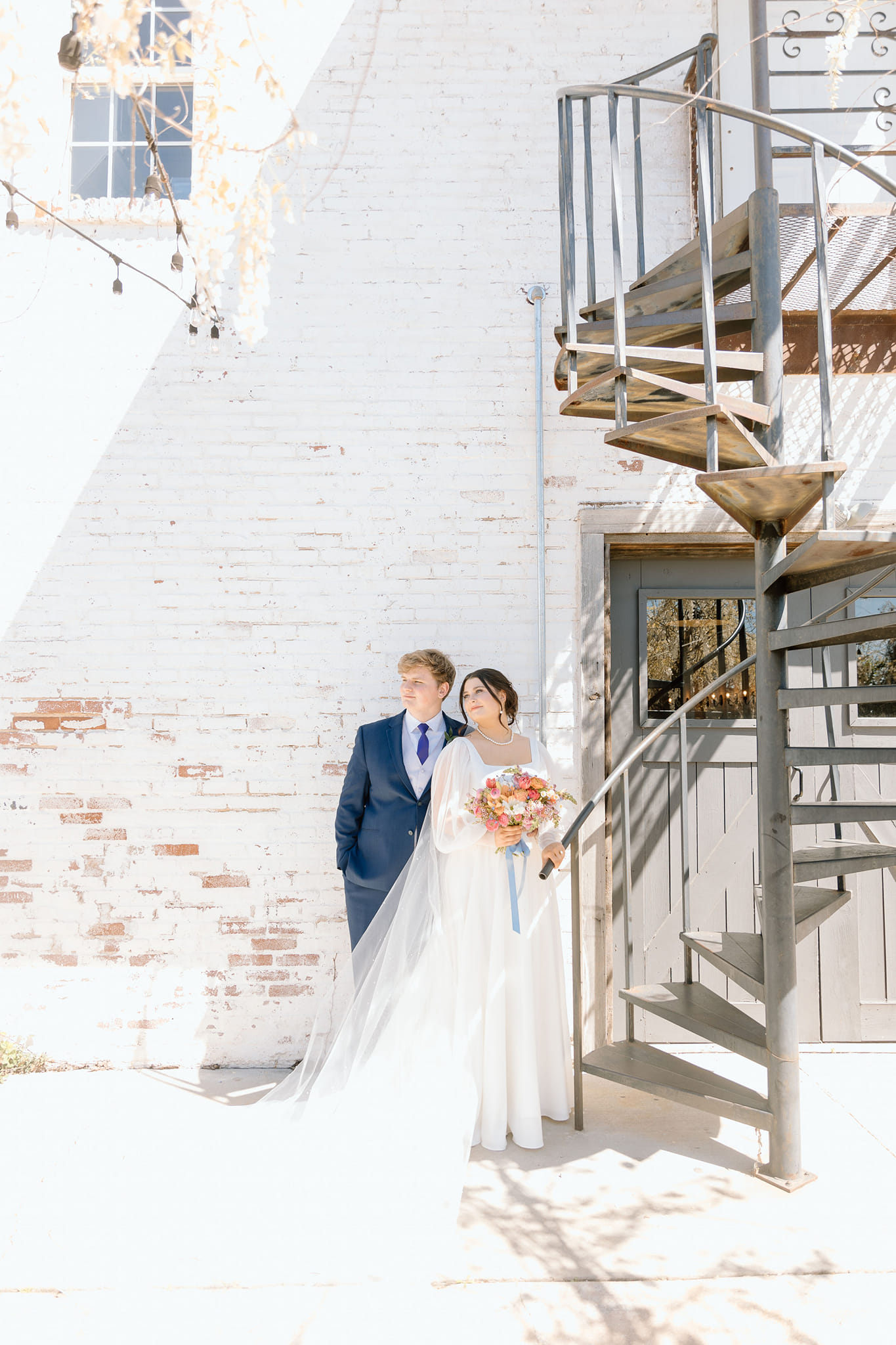 bride and groom posing in front of white brick wall