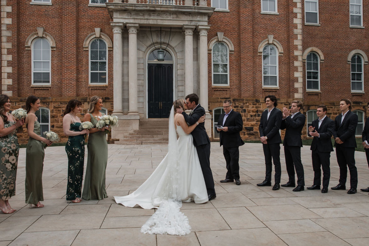 bride and groom kissing while wedding party cheers